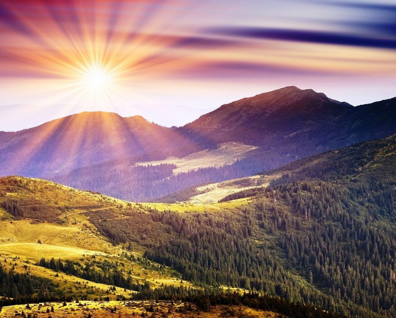 Sunrise shining over rolling mountains with colorful clouds and green valleys.